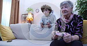 Boy and senior women playing video game on console. Grandmother and grandson playing video games using gamepads at home