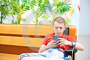 The boy is serious with a smartphone and smart clock is sitting on the bench and looking into the phone.