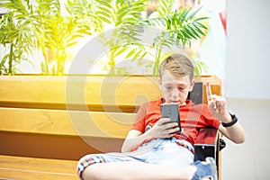 The boy is serious with a smartphone and smart clock is sitting on the bench and looking into the phone. Photo with tinting