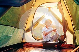 Boy sets up touristic tent ob sunset forest glade