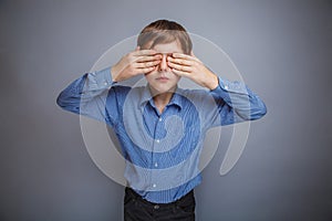 Boy in shirt eyes closed hands on gray background
