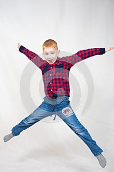 a boy in a shirt and jeans jumped up high with his arms and legs outstretched. he has a big smile on his face