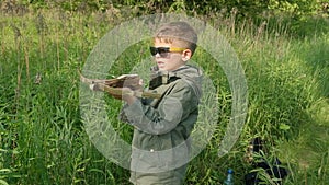 A boy shoots a children's crossbow in a summer forest.