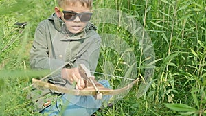 A boy shoots a children's crossbow in a summer forest.