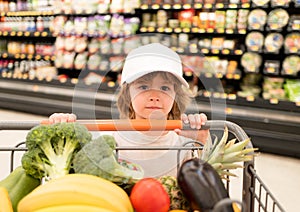 A boy is shopping in a supermarket. Funny customer boy child holdind trolley, shopping at supermarket, grocery store.