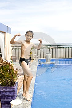 Boy showing his muscle besides swimming pool