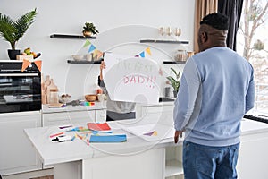 Boy showing placard to his daddy while congratulating him with Fathers Day at the kitchen