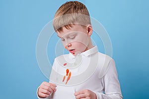 Boy showing a red stain spilled from tomato sauce on white clothes. The concept of cleaning stains on clothes.