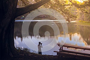 Boy silhouette photographing a beautiful sunset on a lake in to the forest