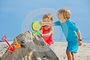 Boy and sister girl play with sand pour water from bucket
