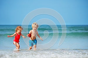 Boy and sister girl run on the sand beach smiling over sea waves