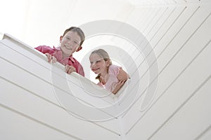 Boy With Sister Looking Over White Wall