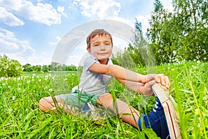 Boy sit on a grass and does gymnastics