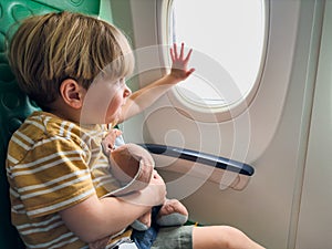 Boy sit near window in the plane hug plush toy holding porthole