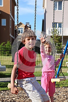 Boy sit on swing and girl waves her hand