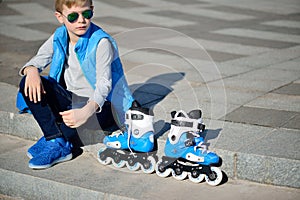 Boy siting with inline roller skates at outdoor skate park