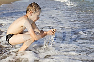 The boy sits on the beach and plays with the wave.