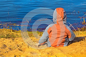 The boy sits on the beach in the sand and looks out to the sea. concept of the flag of Ukraine new generation