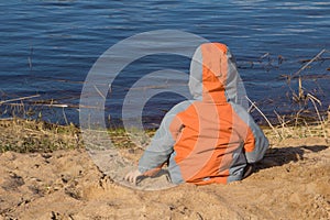 The boy sits on the beach in the sand looks out to the sea. concept flag of Ukraine and the new generation looking to the future