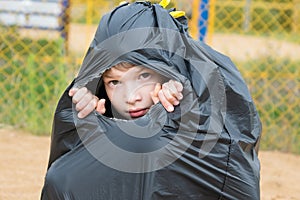 Boy sits in a big black garbage bag and looks through a hole in it, abandoned children concept