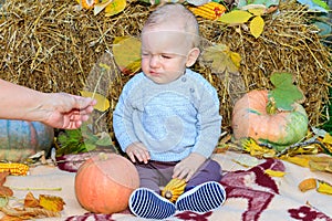 The boy sits on a blanket next to a pumpkin and cries. The boy is sad and unhappy. Autumn season