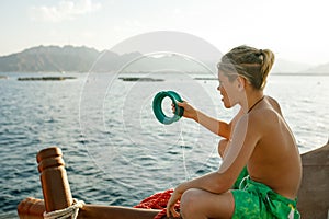 A boy sits on a boat with a reel of fishing line in his hands, on the high seas, looks into the distance, prepares to fish