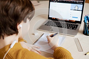 boy sits in class on his laptop at an online school and watches as the teacher