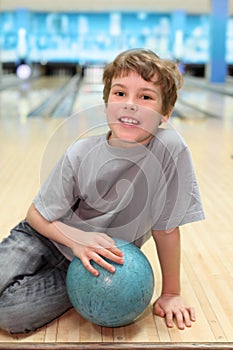 Boy sits on floor with ball in bowling club