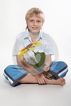 A boy sits on a floor with a sunflower in hands. He is happy.