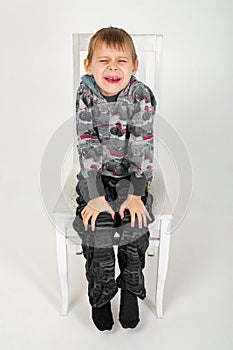 The boy sits and grimaces on a chair on a white background