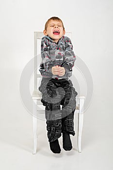 The boy sits and grimaces on a chair on a white background