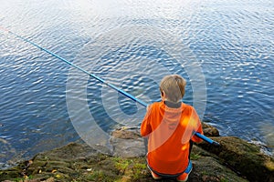 the boy sits with his back and catches fish with a fishing rod in the river