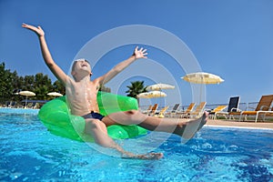 Boy sits on an inflatable arm-chair in pool