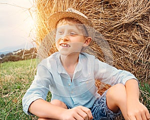 Boy sits near big haystack on the field