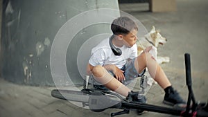 The boy sits in the park after falling off a bicycle, calms the pain in his knee, represents a dangerous bike riding