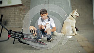 The boy sits in the park after falling off a bicycle, calms the pain in his knee, represents a dangerous bike riding