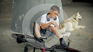 The boy sits in the park after falling off a bicycle, calms the pain in his knee, represents a dangerous bike riding