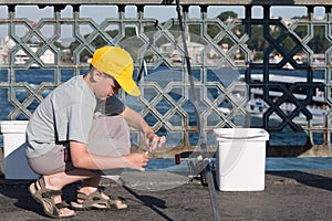 The boy sits and puts bait on hook