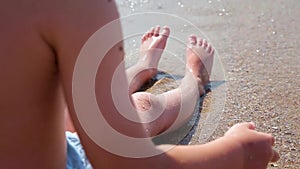 A boy sits by the sea and catches waves. The waves wash the boy`s feet. Sea vacation for family with kids.