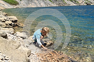 boy sits on shore of blue karst lake in the mountains