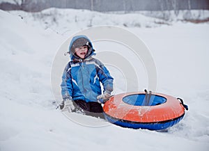 The boy sits in the snow , holding the tubing