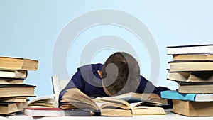 Boy sits at the table and falls asleep for a book. Blue background