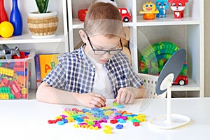 The boy sits at the table and makes words out of letters