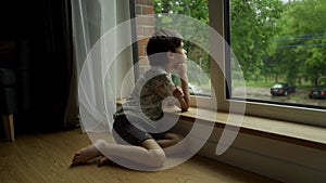 A boy sits at a wet window during the rain and looks at the street