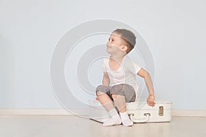 The boy sits on the white suitcase in the room