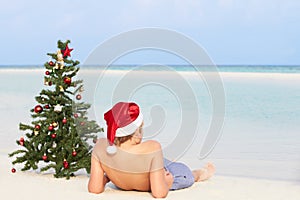 Boy Sitting On Beach With Christmas Tree And Hat