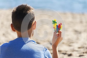 Boy sitting on the beach, looking to the sea ocean and holding colorful autism awareness heart