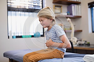 Boy sitting on bed with stomachache photo