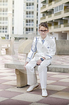 Boy sitting on the bench of an urbanization with his communion suit, prepared for its celebration