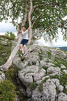 Boy sitting on birch on Lago-Naki plateau in summer